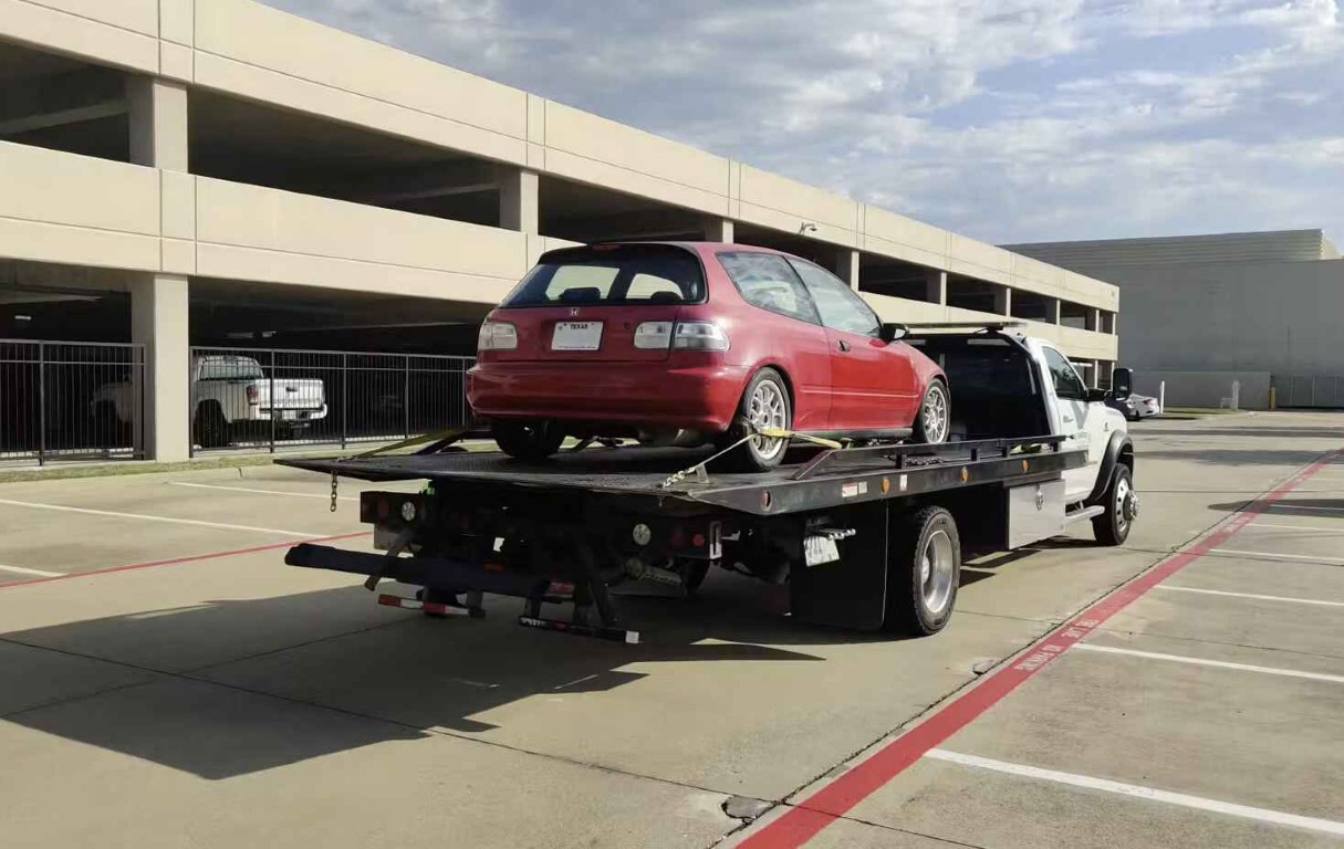 Flatbed tow truck transporting red car for long-distance towing service